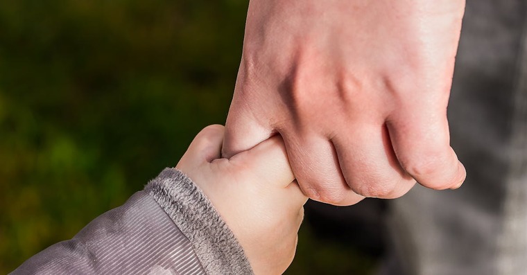 An adult hand gently holds a child's hand outdoors, embodying the supportive presence of a McKenzie Friend in the family court journey.